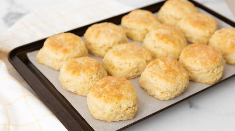 A sheet of hot buttermilk biscuits fresh from the oven over a white counter.
