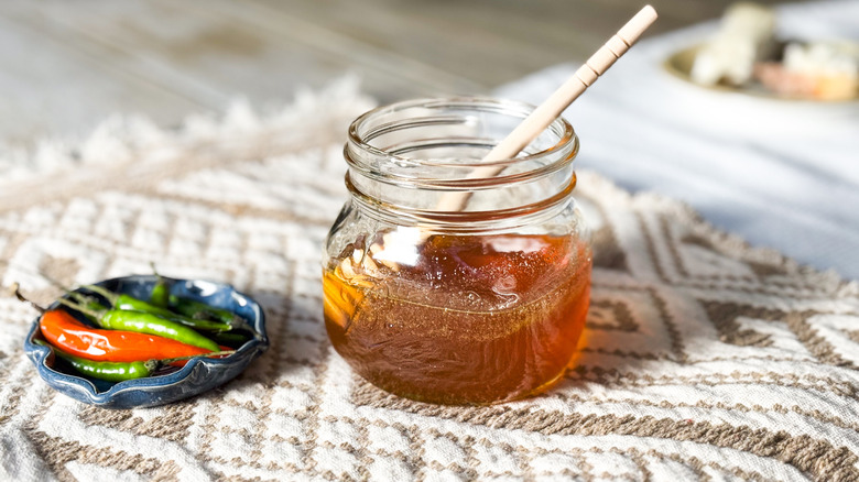 Homemade hot honey in jar with honey dipper and bowl hot hot chiles