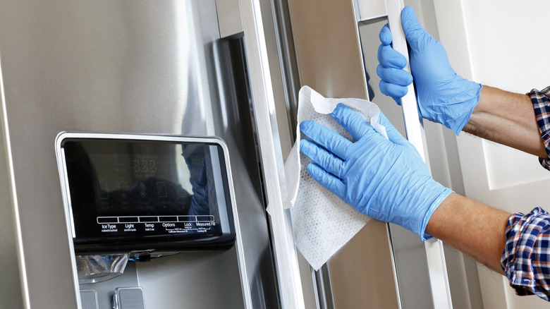 An individual cleaning a steel refrigerator.