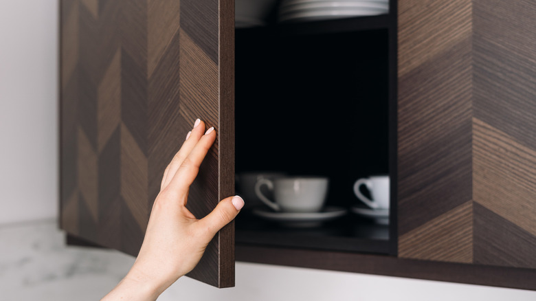 Someone reaches for a high kitchen cabinet.