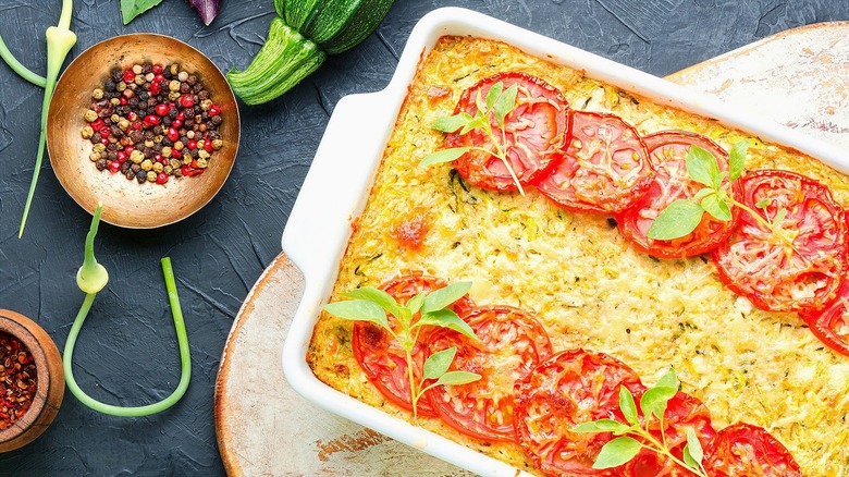 Baked strata in a white casserole dish covered with sliced tomatoes and cheese