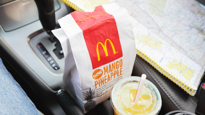 A McDonald's bag sitting on a car's center console near a road map and drink