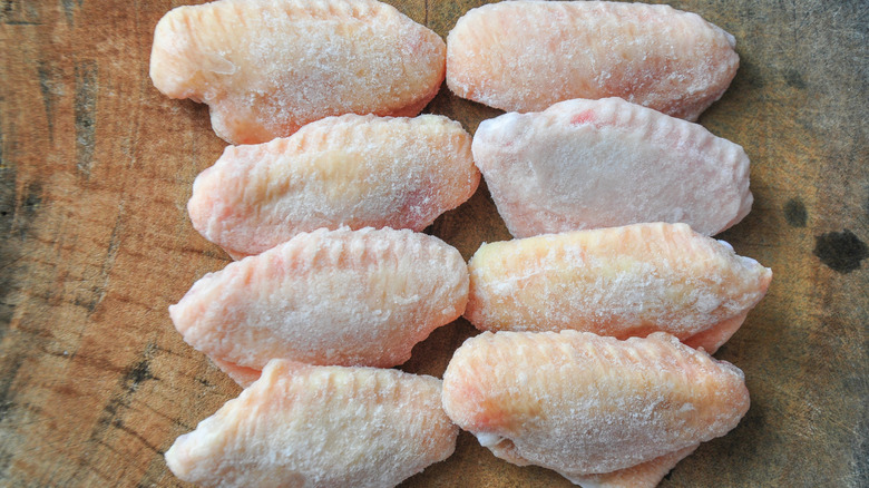 A frozen chicken breast on a wooden cutting board, a knife above it