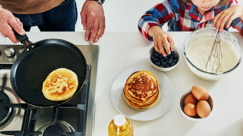High-angle shot of a little boy making pancakes with his father in the kitchen at home