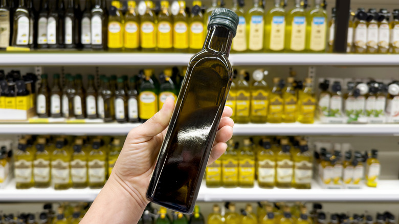 A person holding a bottle of olive oil in front of a supermarket shelf