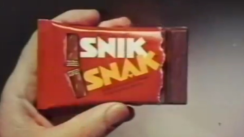 Image from 1970s Snik Snak commercial showing hand holding red Snik Snak package with one segment of chocolate sticking out on the right
