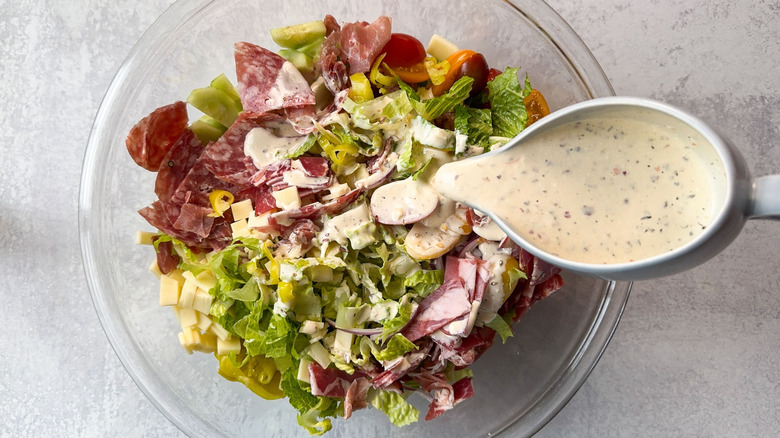 Pouring dressing onto Italian deli grinder salad ingredients in glass bowl
