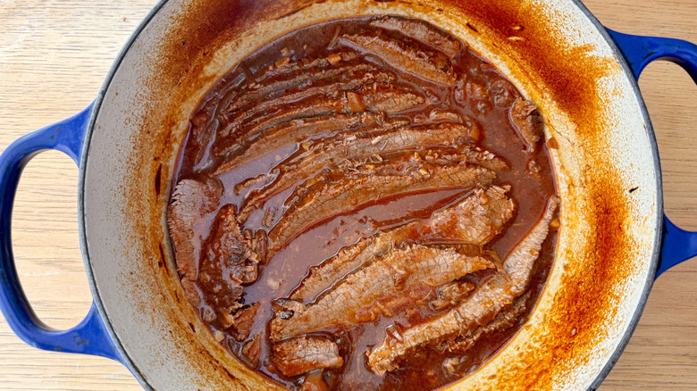 Sliced brisket and sauce in Dutch oven