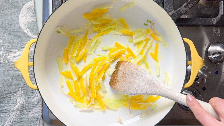 Sauteing yellow bell pepper, fennel bulb, and shallot with a wooden spoon in pan on stovetop