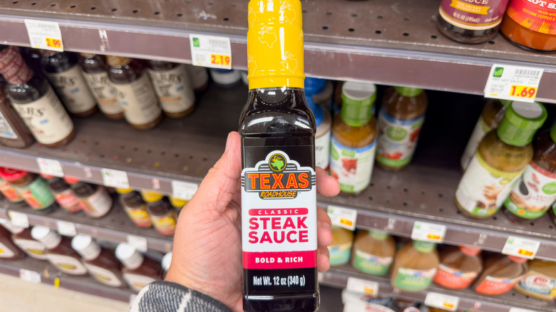 A person holding a bottle of Texas Roadhouse Steak Sauce at a grocery store